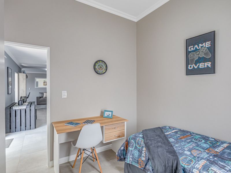 A well-maintained bedroom featuring neutral wall tones, crown molding, and tiled flooring, with a clear view into the adjacent living area.