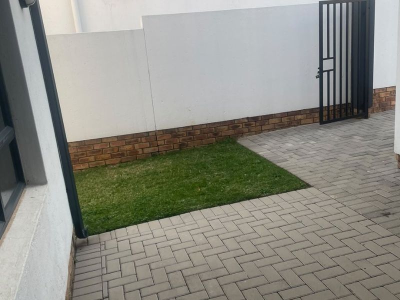 A private rear courtyard featuring paved flooring, a small lawn, and a secure metal pedestrian gate.