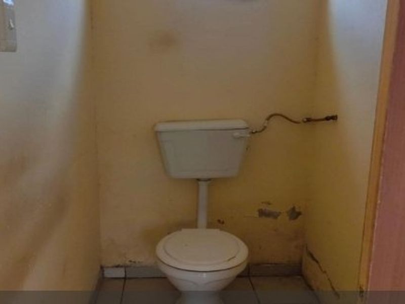 A small, dated bathroom featuring a standard toilet and cistern, requiring significant cosmetic updates and wall repairs.