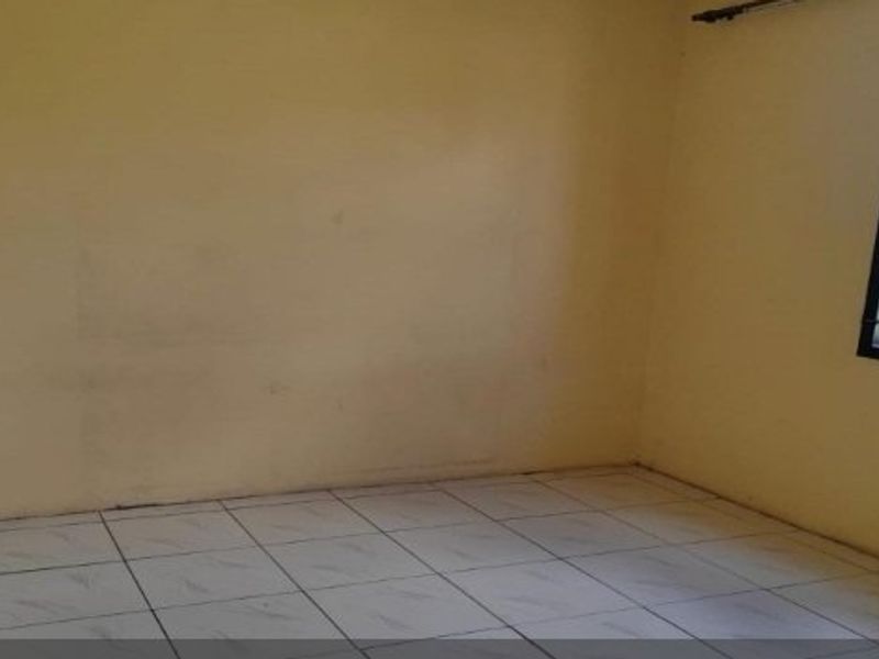 An empty bedroom featuring tiled flooring and a window fitted with security bars, offering a blank canvas for personalization.