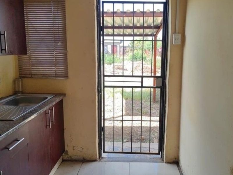 A functional scullery area featuring built-in cabinetry, a stainless steel sink, and direct access to the rear exterior through a security gate.