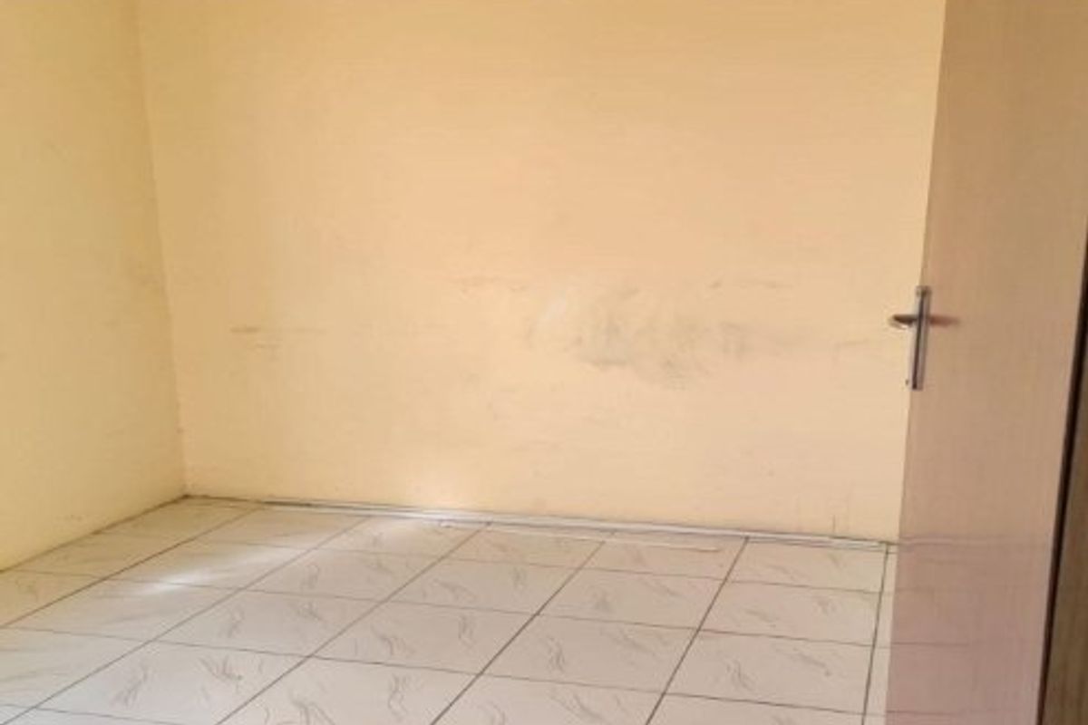 An empty bedroom featuring tiled flooring and plain walls with visible signs of wear and staining.