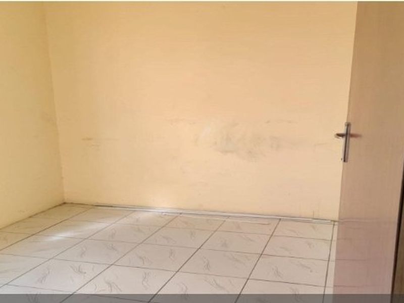 An empty bedroom featuring tiled flooring and plain walls with visible signs of wear and staining.
