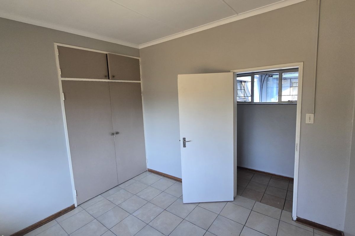An empty bedroom featuring neutral wall paint, tiled flooring, and built-in cupboards with overhead storage compartments.