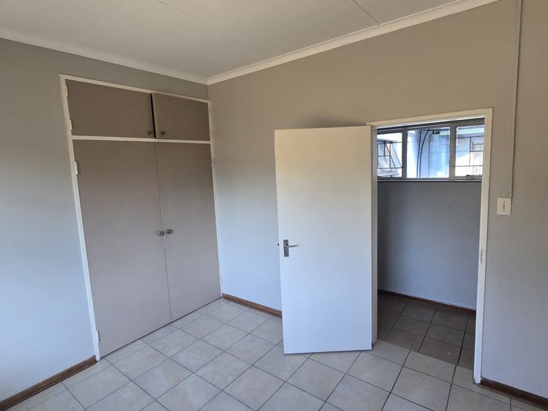 An empty bedroom featuring neutral wall paint, tiled flooring, and built-in cupboards with overhead storage compartments.