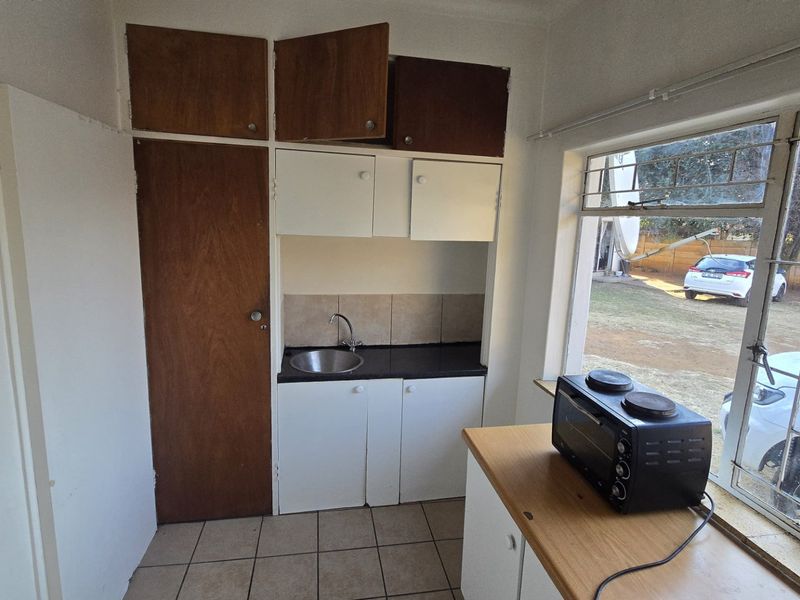 Compact kitchen area featuring built-in cabinetry, a stainless steel sink, tiled backsplash, and tiled flooring with natural light from a large window.