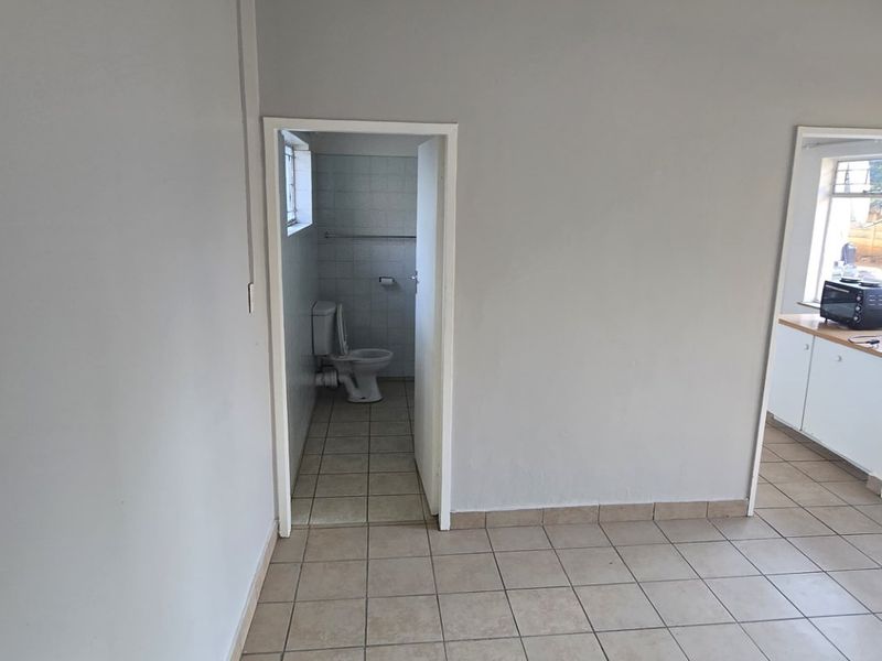 An open-plan living area featuring neutral wall paint and ceramic floor tiles, with direct access to an adjacent bathroom and kitchen space.