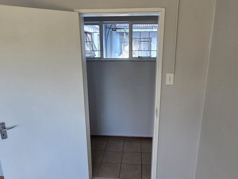 A vacant hallway featuring neutral tiled flooring and a doorway leading to an adjacent space with security-barred windows.