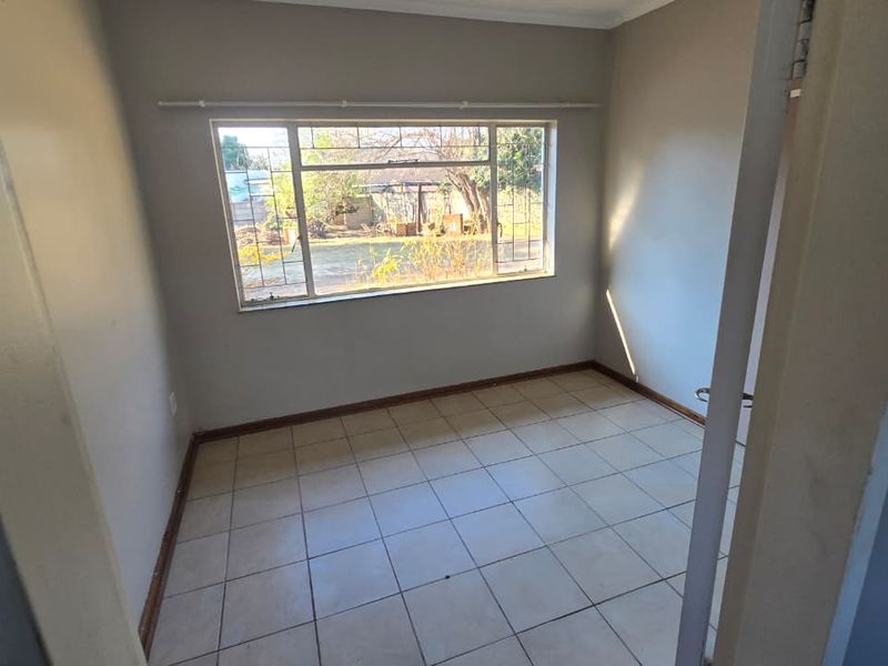 An empty bedroom featuring tiled flooring and a large window, providing a blank canvas for personalization and interior design updates.