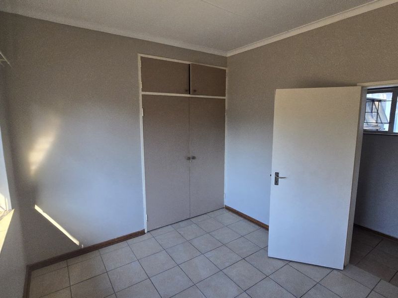 An empty bedroom featuring tiled flooring, built-in cupboards, and natural light from steel-framed windows.