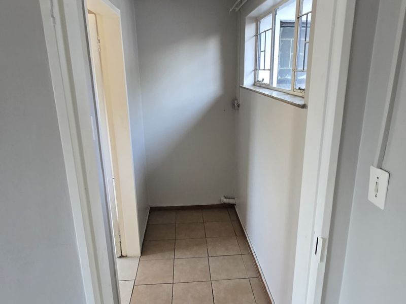 A clean, empty hallway featuring neutral wall paint, tiled flooring, and a window with security bars, providing a bright and functional transition space.