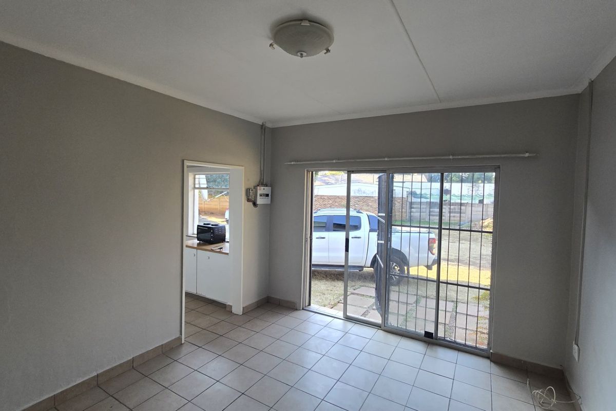 An empty living room featuring tiled flooring, a sliding glass door with security gate, and direct access to an adjacent kitchen area.