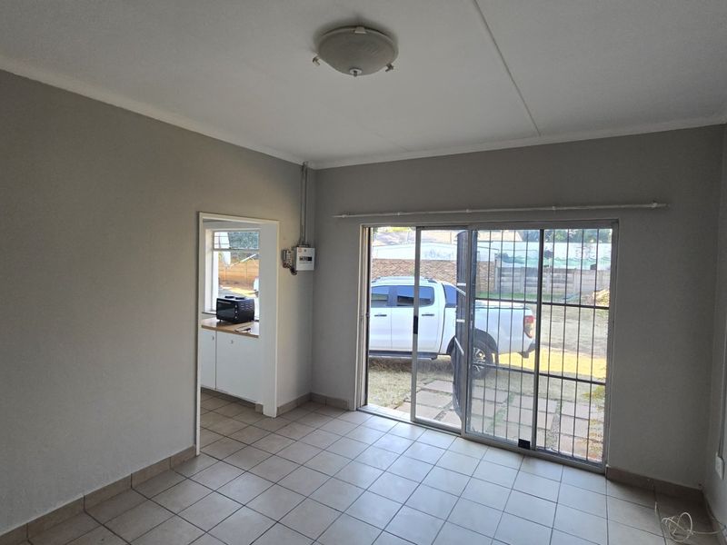 An empty living room featuring tiled flooring, a sliding glass door with security gate, and direct access to an adjacent kitchen area.