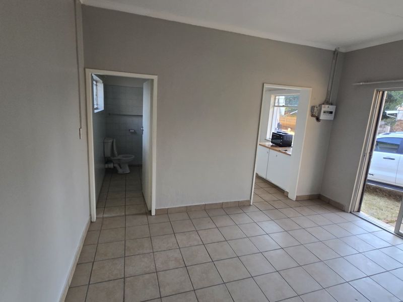 An open-plan living area featuring tiled flooring, a sliding glass door to the exterior, and direct access to an adjacent bathroom and kitchen area.