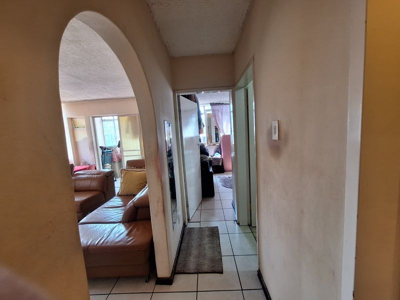 A hallway featuring an arched entryway, ceramic floor tiles, and visible wall wear, providing access to the living area and adjacent rooms.
