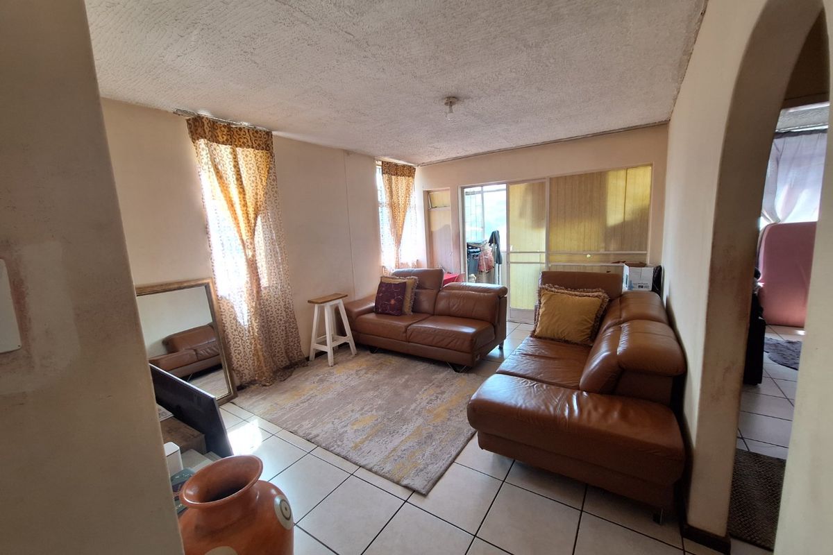 A living room featuring tiled flooring, an arched entryway, and a sliding glass door leading to an outdoor area, showing signs of wear.