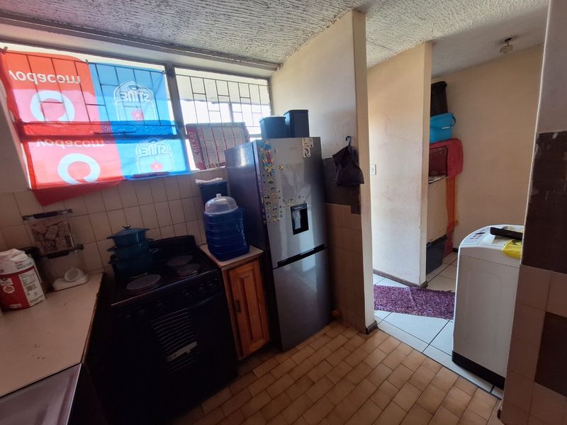 A functional kitchen area featuring tiled flooring, a tiled backsplash, and textured ceilings, requiring cosmetic updates to improve its overall condition and appeal.