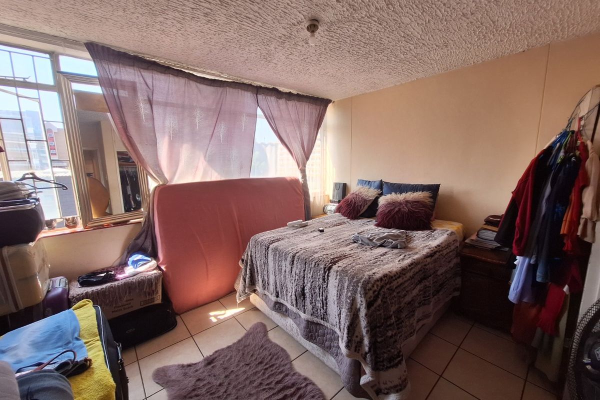 A bedroom featuring tiled flooring, a textured ceiling, and a large window with security bars, requiring cosmetic updates to improve its overall condition.