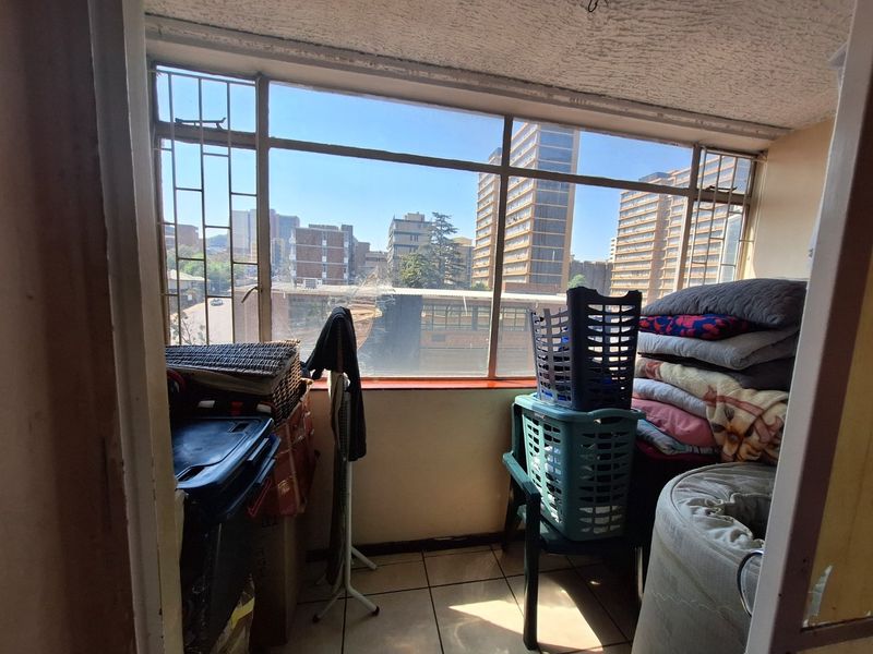 Enclosed balcony area featuring tiled flooring and large windows with security bars, offering an urban city view.