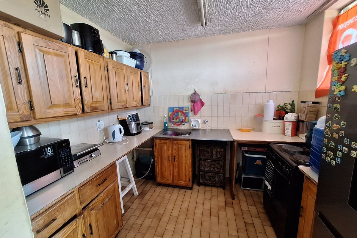 A dated kitchen featuring wooden cabinetry, laminate countertops, a stainless steel sink, and a tiled backsplash, offering potential for a modern renovation.