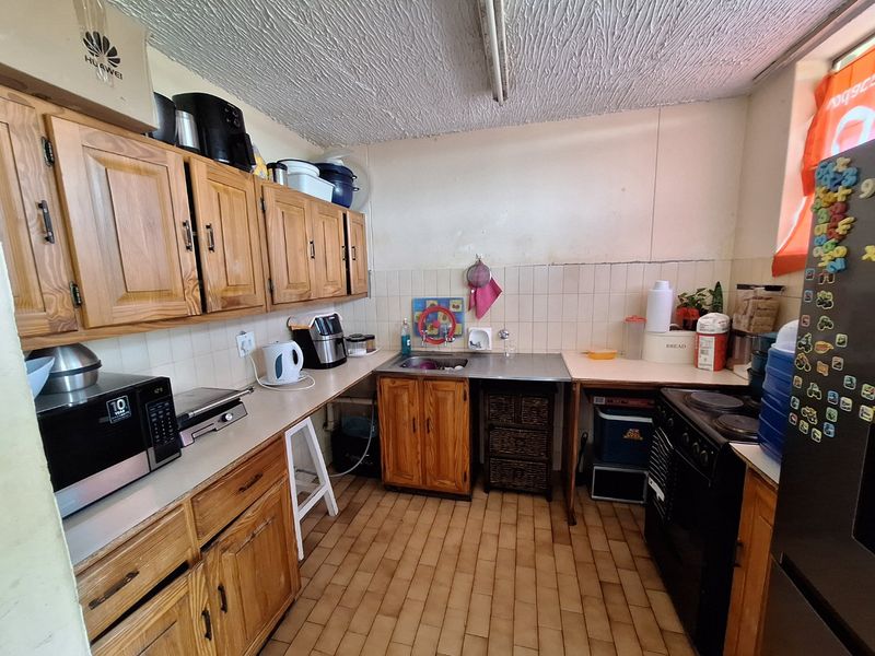 A dated kitchen featuring wooden cabinetry, laminate countertops, a stainless steel sink, and a tiled backsplash, offering potential for a modern renovation.