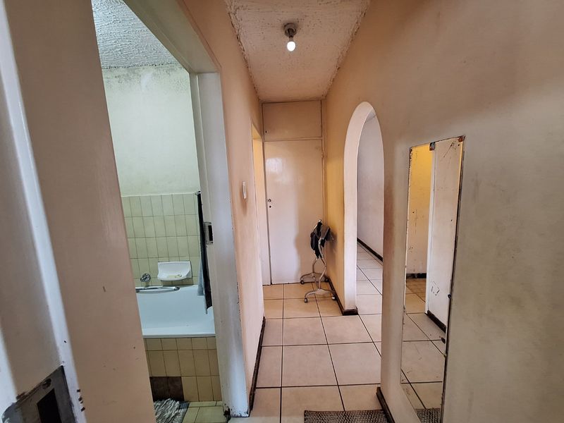 A dated hallway featuring tiled flooring, an arched entryway, and a built-in cupboard, requiring cosmetic updates to improve its overall condition.