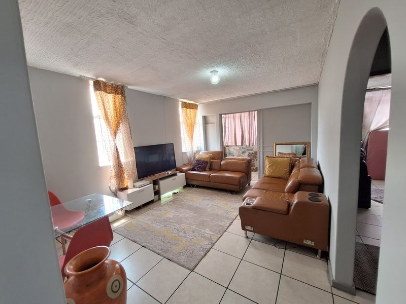 A living room featuring tiled flooring, an arched entryway, and a textured ceiling, offering a functional space with potential for modern updates.
