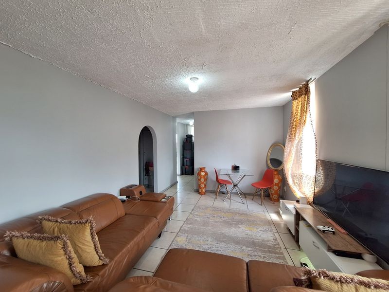 A living room featuring tiled flooring, an arched doorway leading to an adjacent space, and a textured ceiling finish.