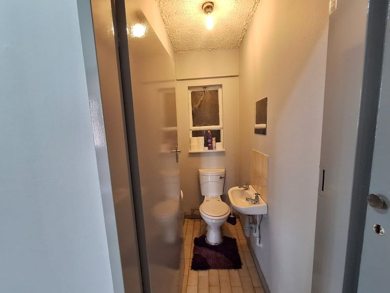 A compact, functional bathroom featuring a standard toilet, wall-mounted basin, and tiled flooring, offering a basic layout ready for modernization.
