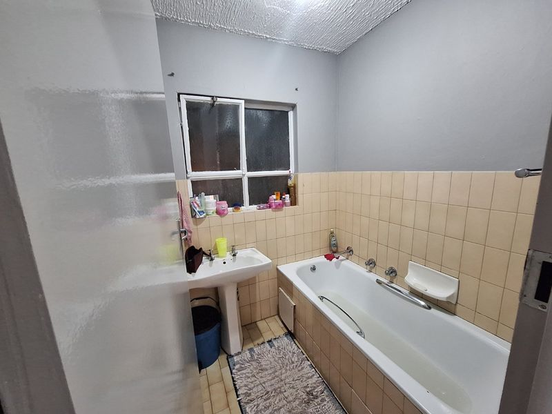 A functional bathroom featuring a pedestal washbasin, a standard bathtub with tiled surround, and tiled flooring.
