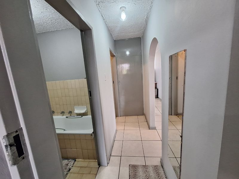 A hallway leading to a bathroom featuring a built-in bathtub with ceramic wall tiles and tiled flooring throughout.