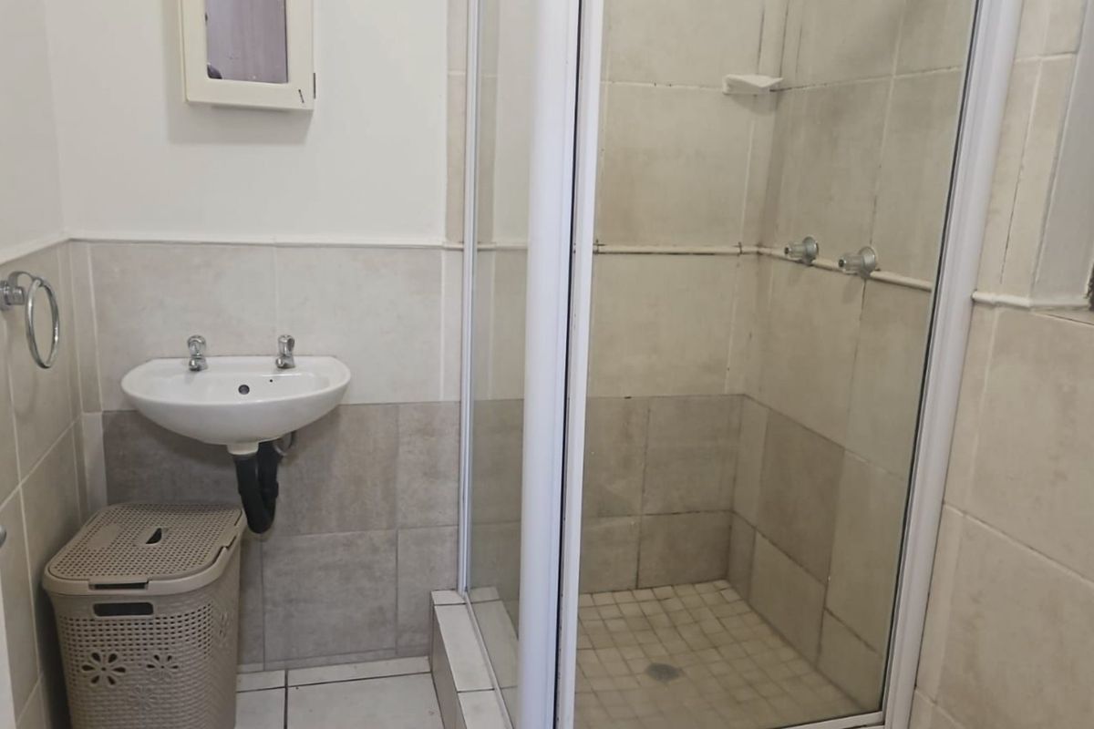 A functional bathroom featuring a shower enclosure and a wall-mounted basin with neutral wall and floor tiling.