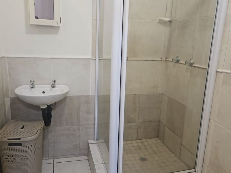A functional bathroom featuring a shower enclosure and a wall-mounted basin with neutral wall and floor tiling.