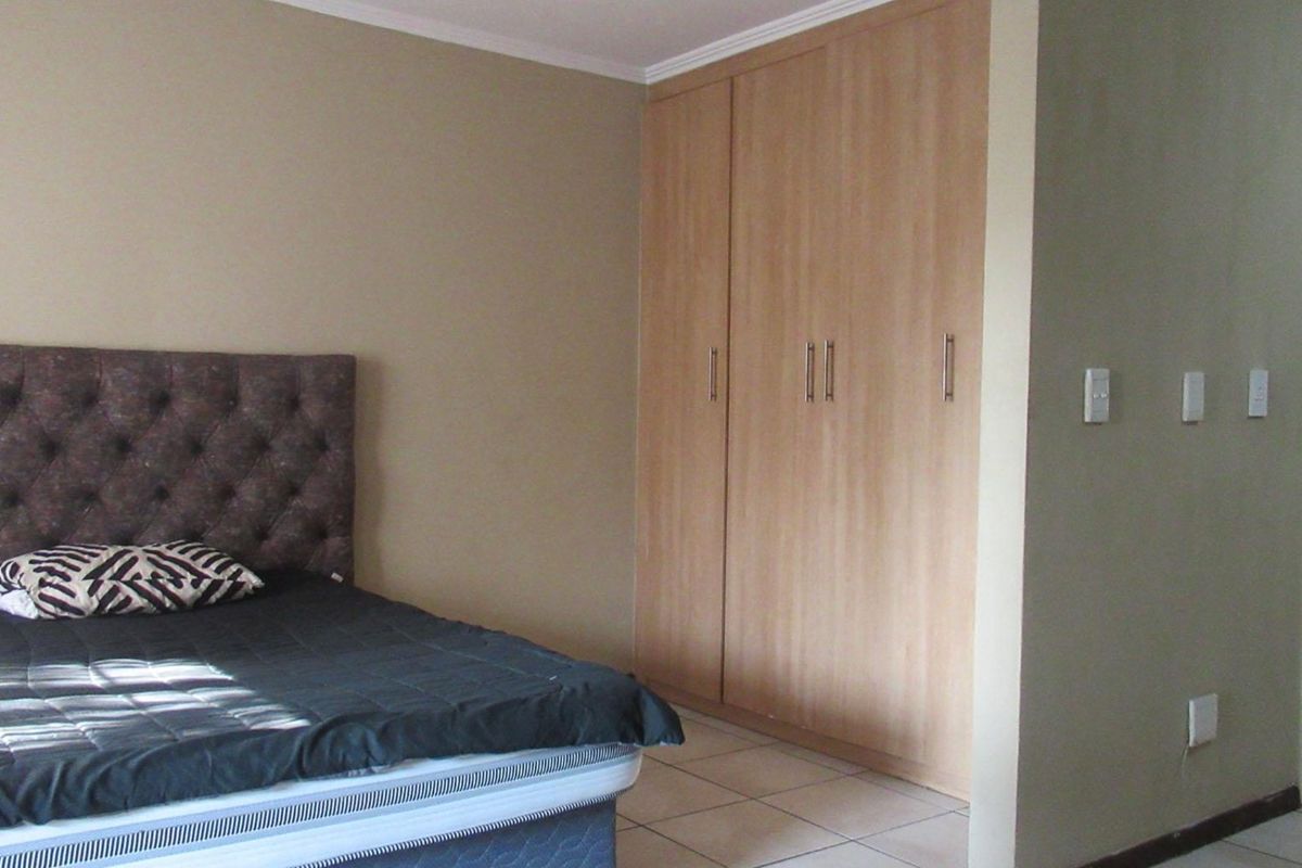 A bedroom featuring built-in wooden cupboards, tiled flooring, and direct access to an en-suite bathroom.