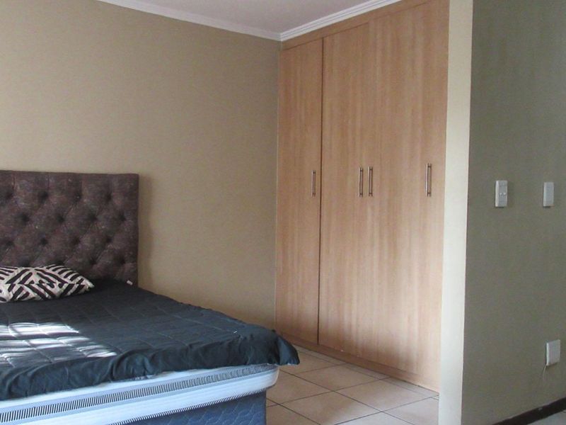 A bedroom featuring built-in wooden cupboards, tiled flooring, and direct access to an en-suite bathroom.