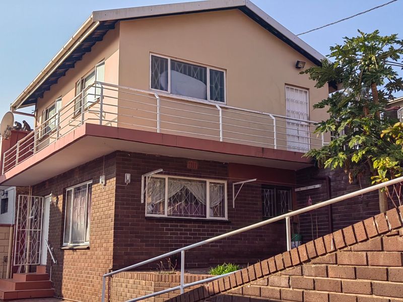 Two-story residential house featuring a brick lower level, upper-level balcony with metal railings, and external brick staircase access.