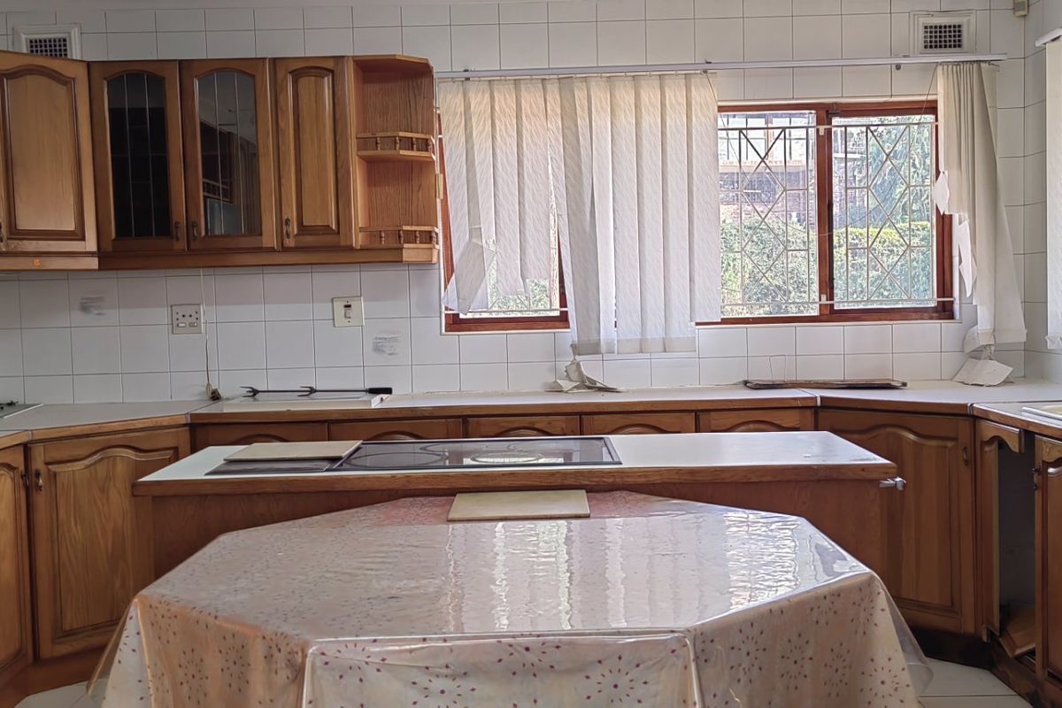 A dated kitchen featuring traditional wooden cabinetry, tiled backsplash, and a central island with a built-in hob, offering potential for modern renovation.