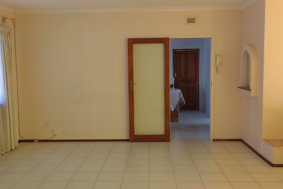 A spacious, empty living area featuring neutral tiled flooring, an arched wall detail, and an intercom system, providing a blank canvas for interior design.