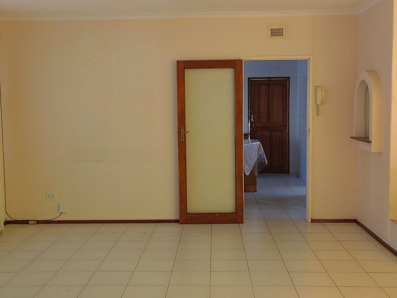 A spacious, empty living area featuring neutral tiled flooring, an arched wall detail, and an intercom system, providing a blank canvas for interior design.