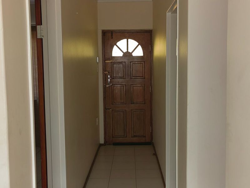 A simple, functional hallway featuring tiled flooring and a traditional timber front door with an arched glass panel.