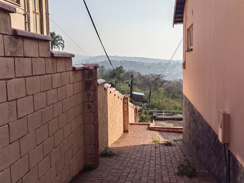 A side pathway featuring paved flooring and a retaining wall, leading towards an open outdoor area with distant landscape views.
