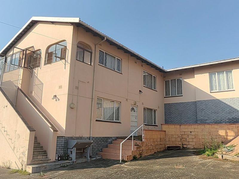 Rear view of a multi-level residential property featuring an external staircase, paved courtyard area, and brick boundary walls.