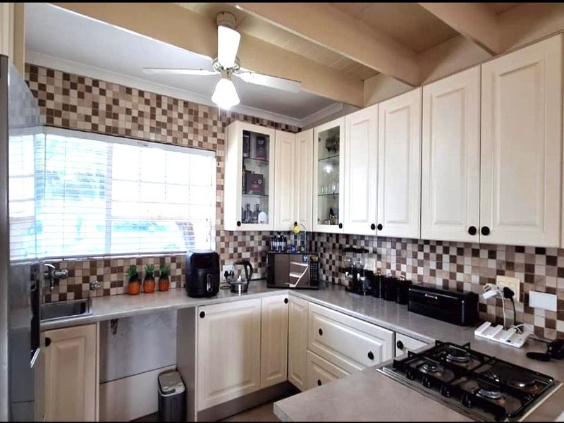 A functional kitchen featuring white cabinetry, a gas cooktop, tiled backsplash, and a ceiling fan, offering a practical layout for daily meal preparation.