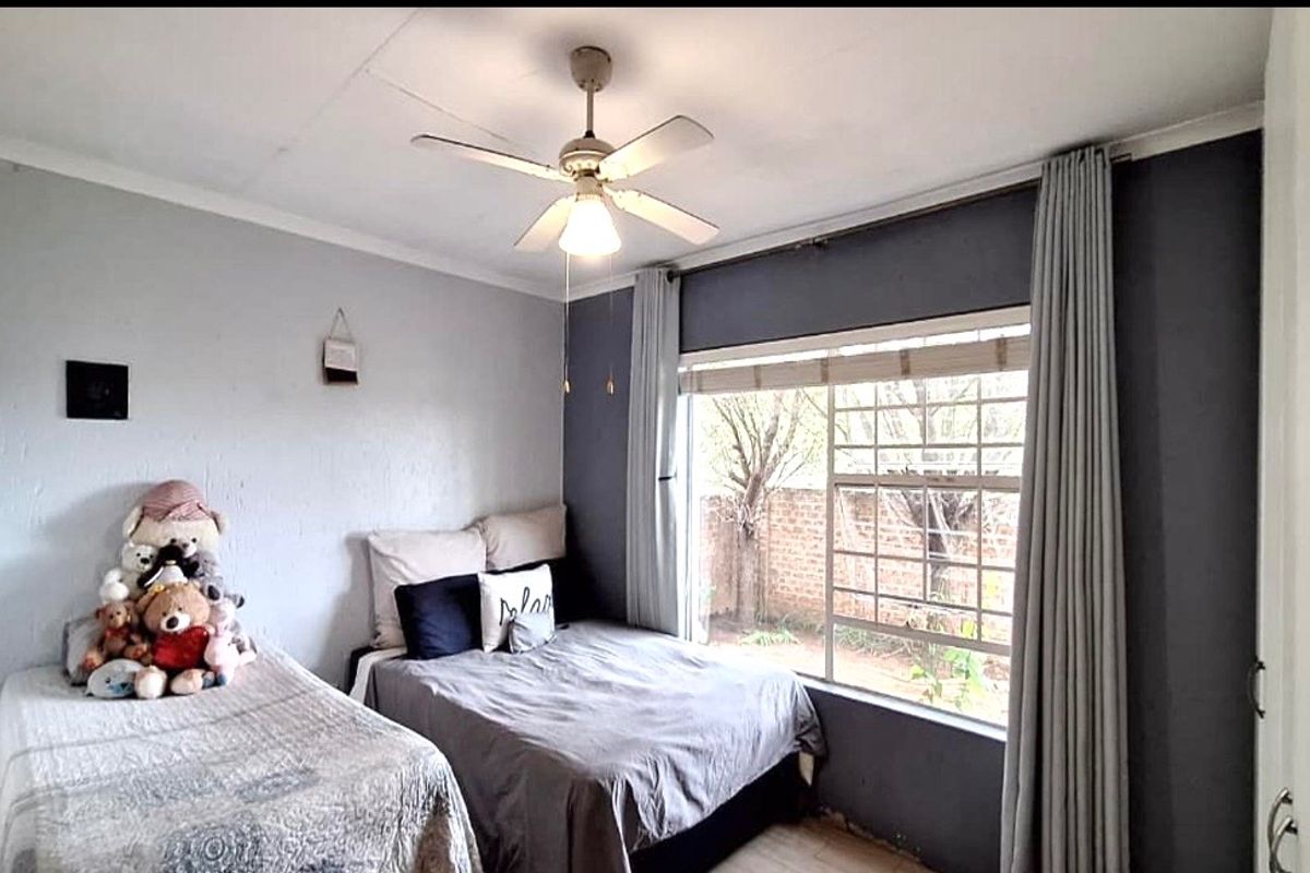 A bedroom featuring a ceiling fan, built-in storage, and a large window with security bars overlooking the rear garden area.