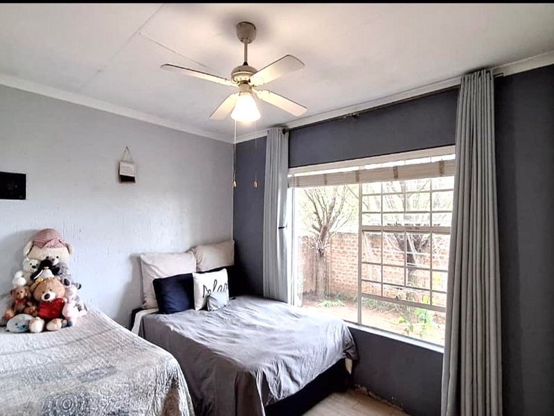 A bedroom featuring a ceiling fan, built-in storage, and a large window with security bars overlooking the rear garden area.