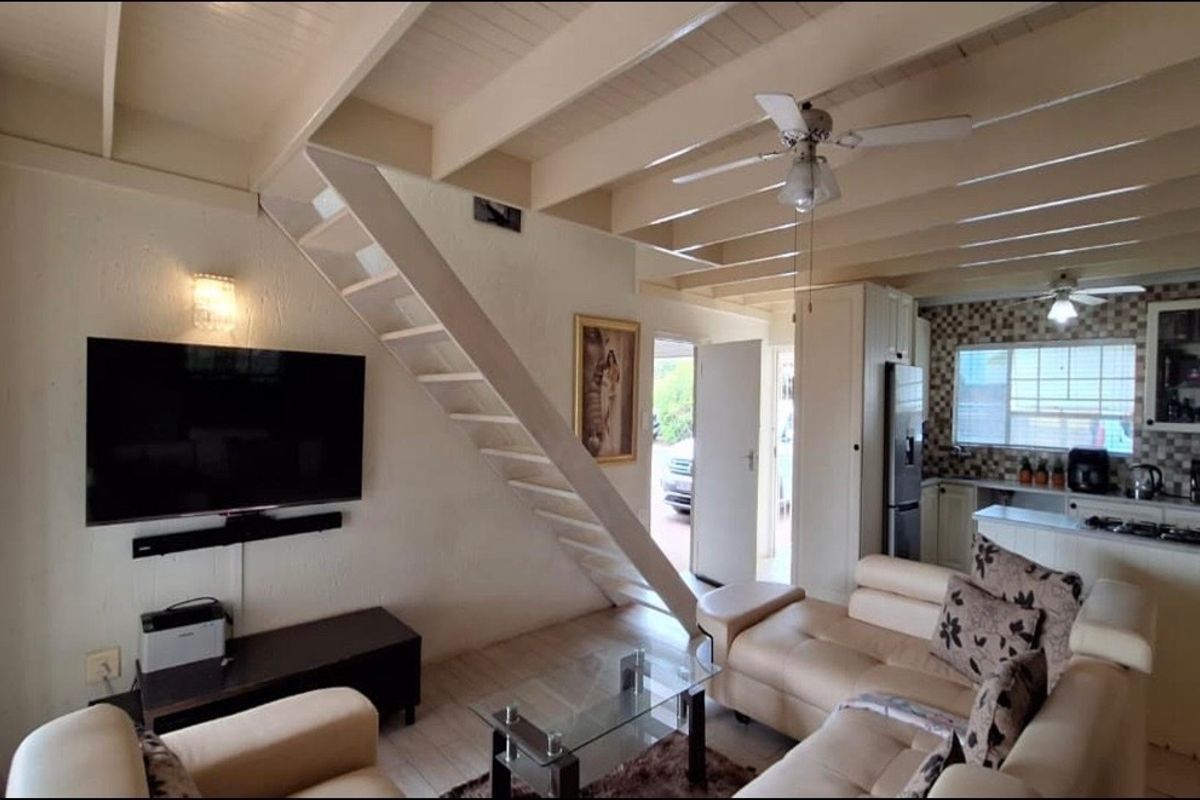 Open-plan living area featuring exposed beam ceilings, a staircase, and an integrated kitchen with tiled backsplash and built-in cabinetry.