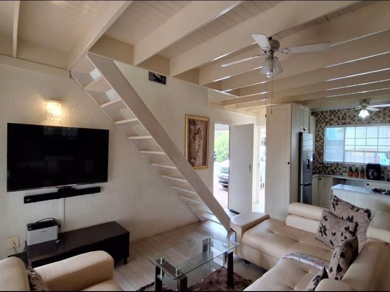 Open-plan living area featuring exposed beam ceilings, a staircase, and an integrated kitchen with tiled backsplash and built-in cabinetry.