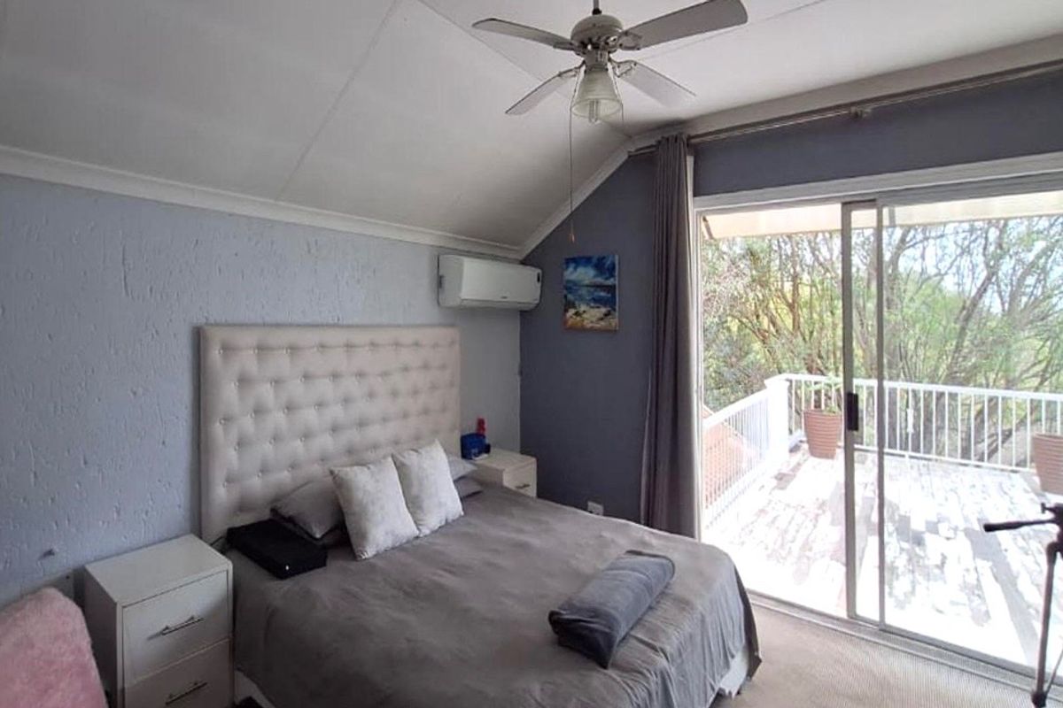 A bedroom featuring a vaulted ceiling, ceiling fan, split-system air conditioning, and sliding glass doors providing direct access to an outdoor balcony.