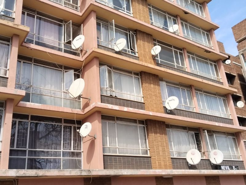 Exterior view of a multi-story apartment building featuring brick and painted concrete facade with multiple satellite dish installations and ground-level garage access.