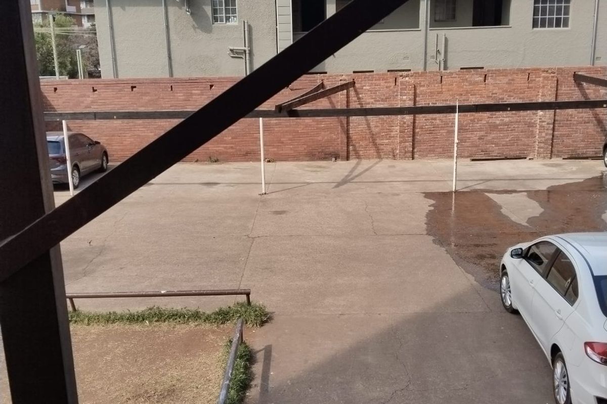 View of the rear exterior area featuring a concrete parking space, brick boundary wall, and metal carport structure.